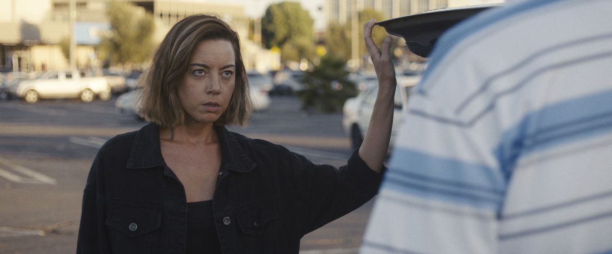 אוברי פלאזה בתפקיד אמילי עומדת ליד תא המטען של מכוניתה, בוהה בקונה פוטנציאלי ב"אמילי הפושעת"